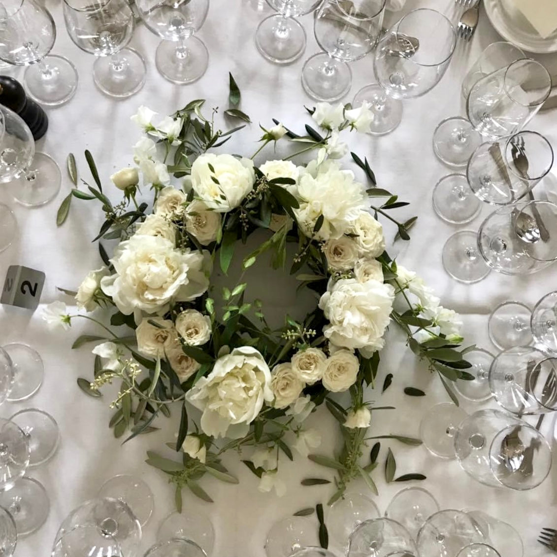 foto taget oppefra : rundpyntet hvid blomster krans på bord. Omkring ses service opdækning.