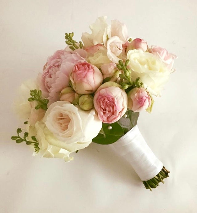 brudebuket i lyserøde og vide farveer med roser. Hvidt skaft hvor stilkene ses forneden.