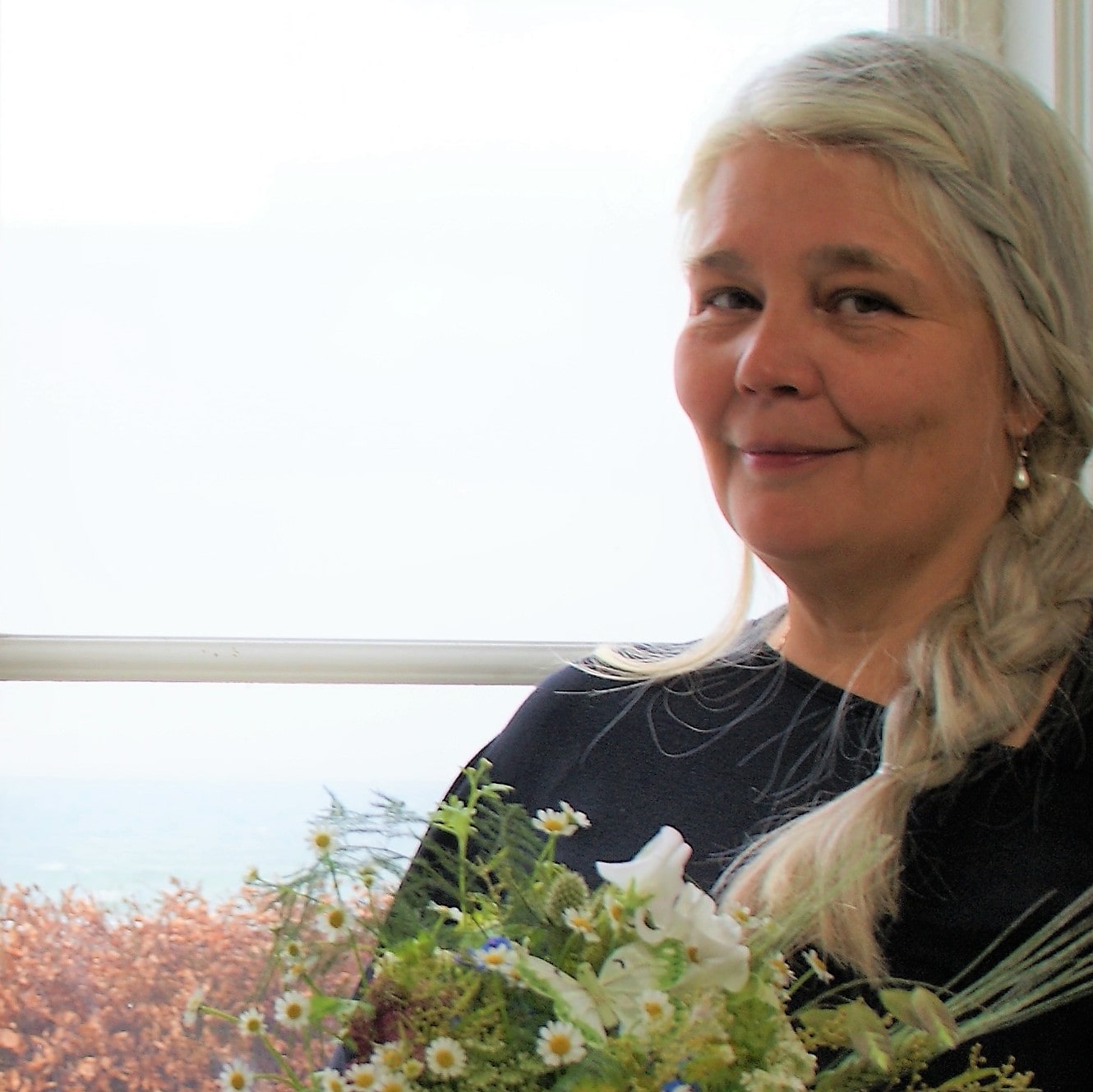 Dekoratør Charlotte Bagge sidder i vinduet på Sophienberg slot med en blomsterbuket og smiler til kameraet.